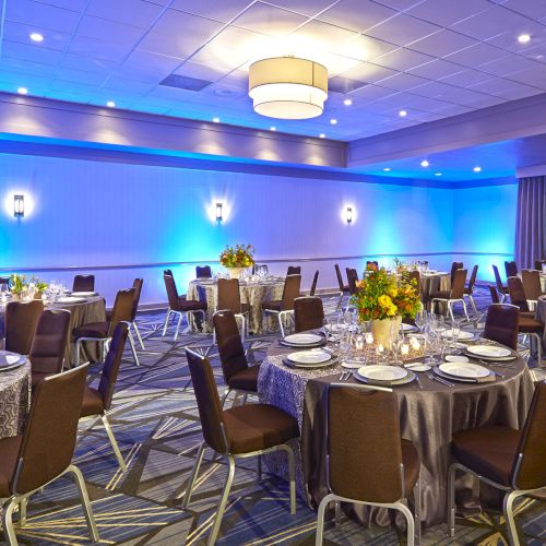 Looks like a banquet hall or conference room with round tables, a stage, blue lighting, and a seated audience.