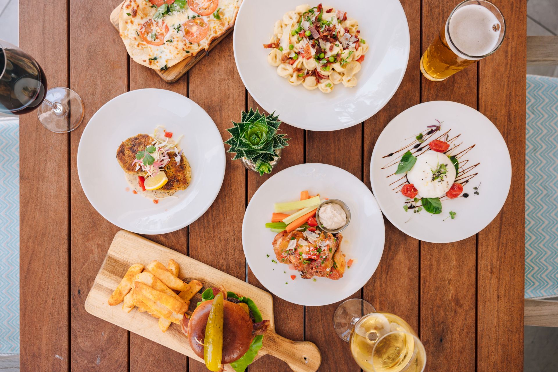 A top-down table spread of gourmet dishes&mdash;pizza, pasta, steak, salad, fries&mdash;and drinks with wine and sauce.