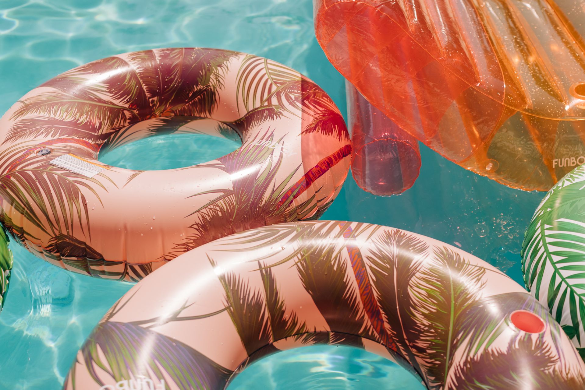 A sunny pool scene with a tropical inflatable palm float, another orange tube, and clear blue water.