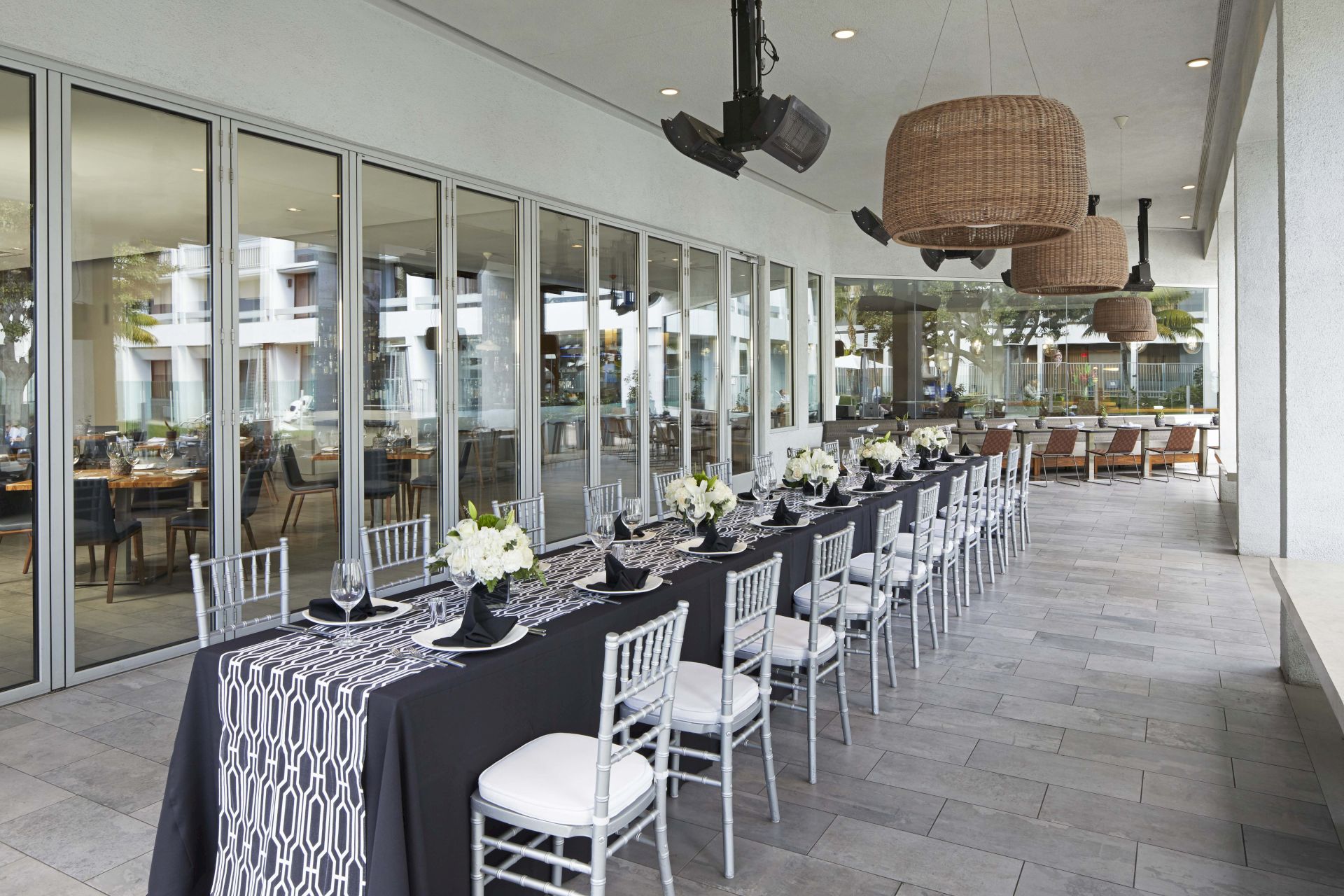Outdoor event patio set up with neatly arranged tables, chairs, candles, and flowers under hanging ceiling fans.